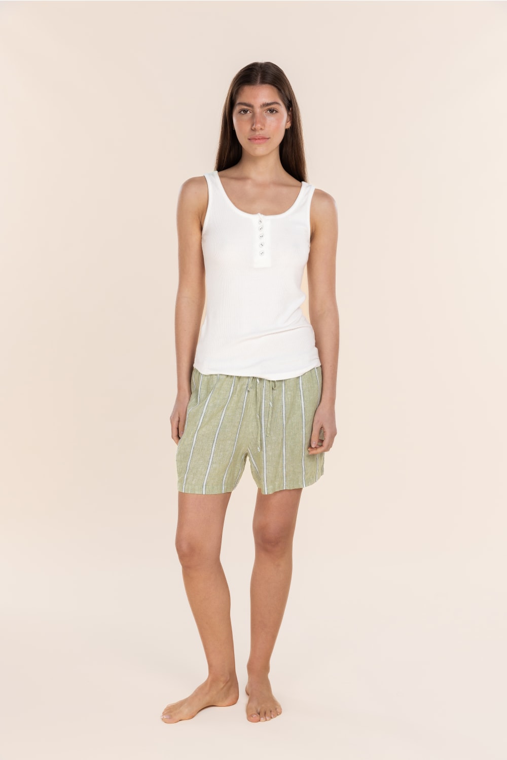 Woman wearing a white tank top and green striped shorts on a beige background