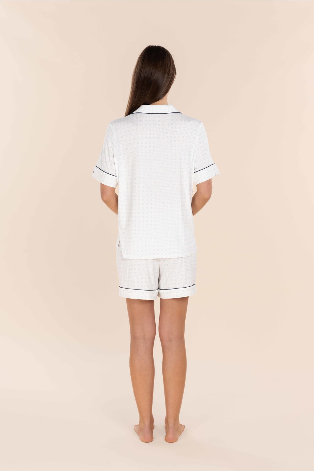 Person wearing a white pajama set with black piping on a beige background