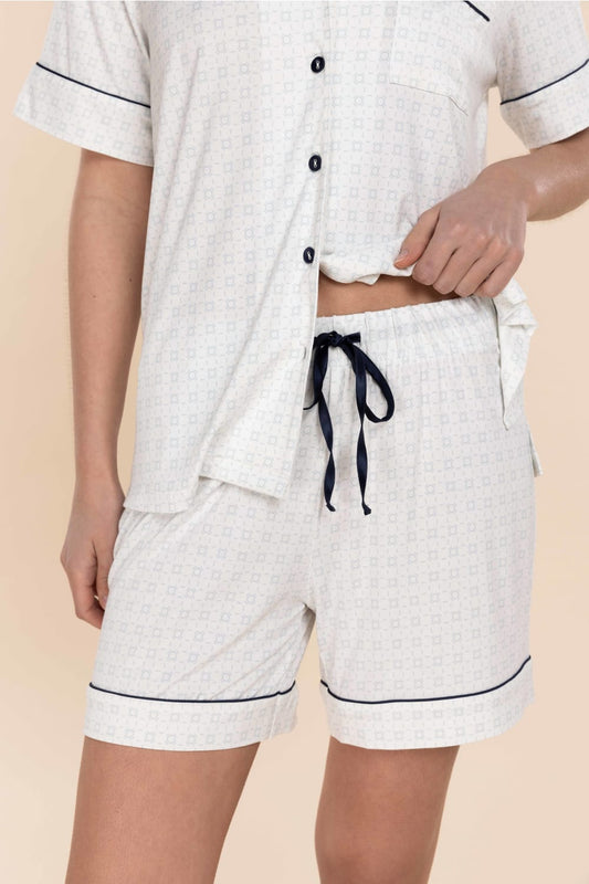 Person wearing a white pajama set with black piping on a beige background