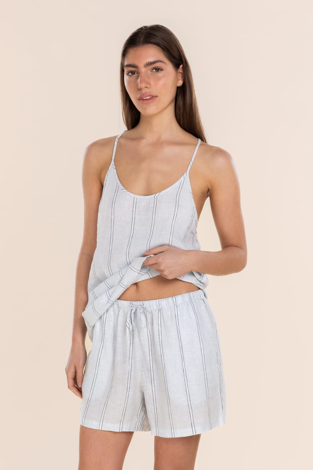 Woman wearing a light blue striped tank top and shorts on a beige background