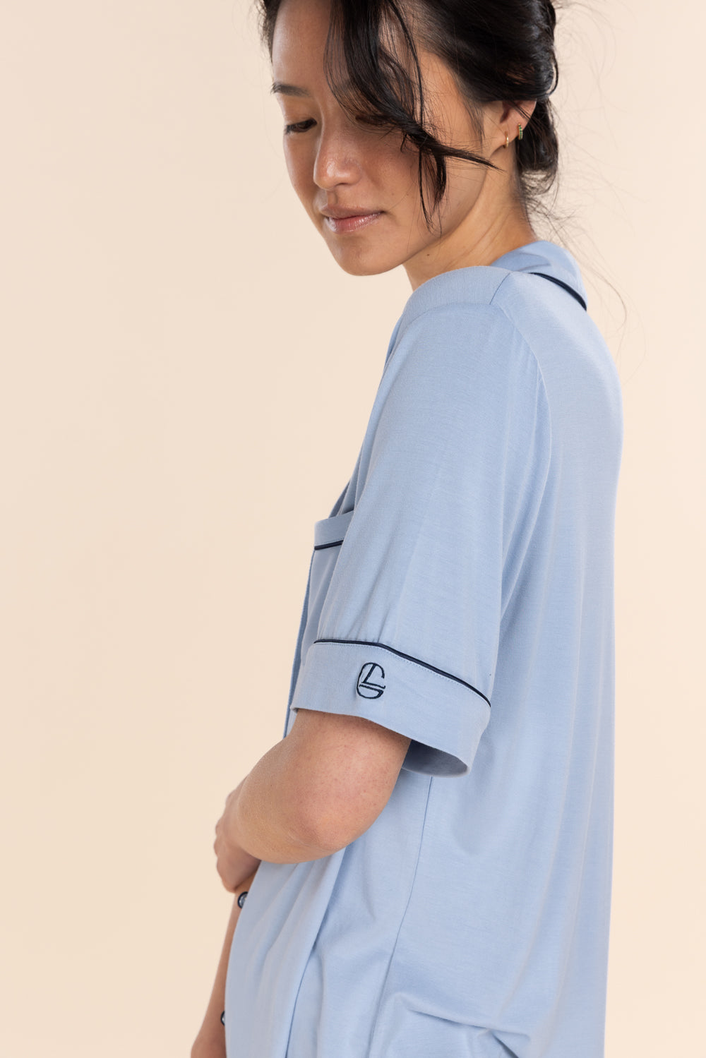 Woman wearing a light blue shirt with a logo on a beige background
