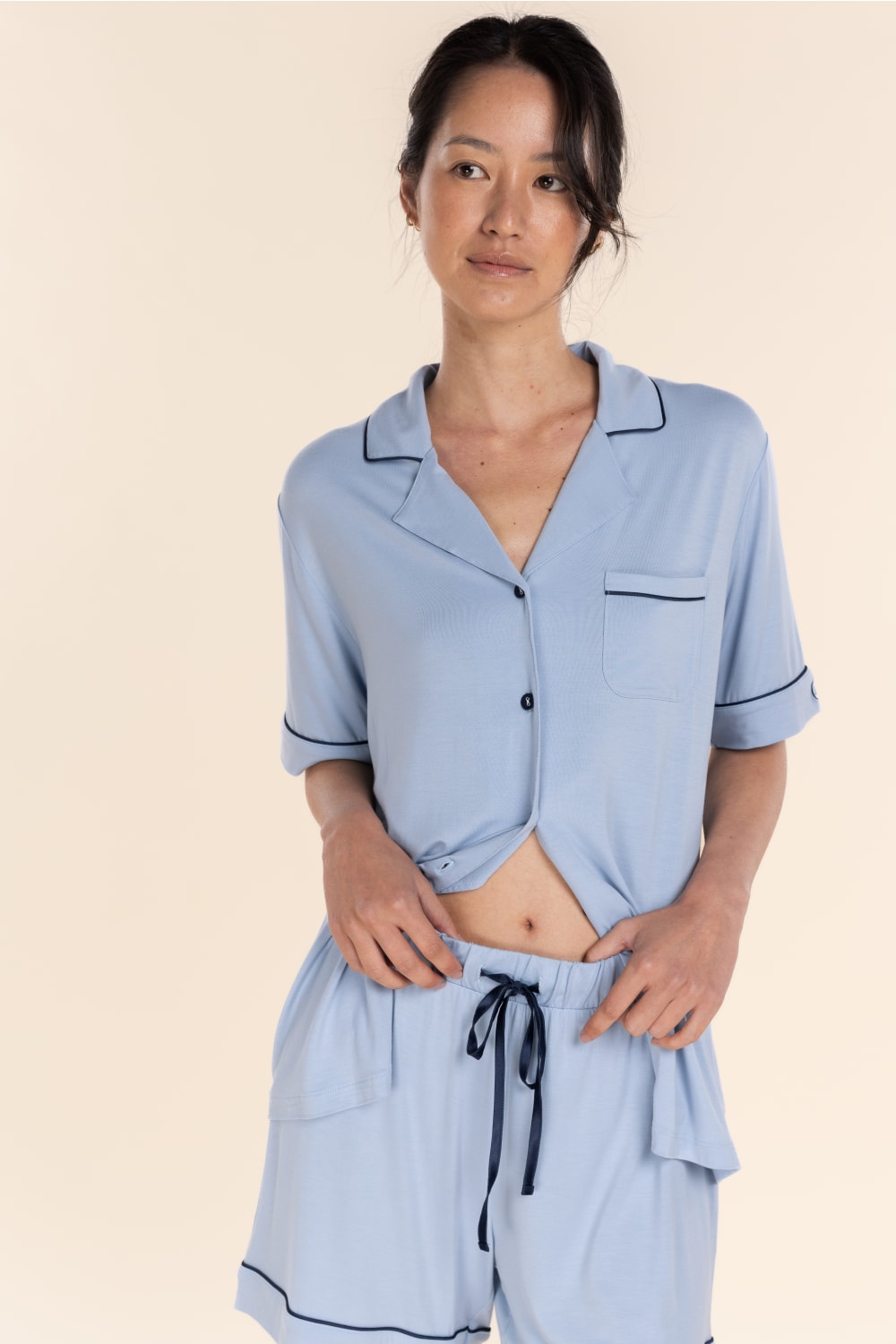 Woman wearing a light blue pajama set with black piping on a beige background