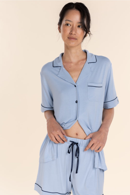 Woman wearing a light blue pajama set with black piping on a beige background