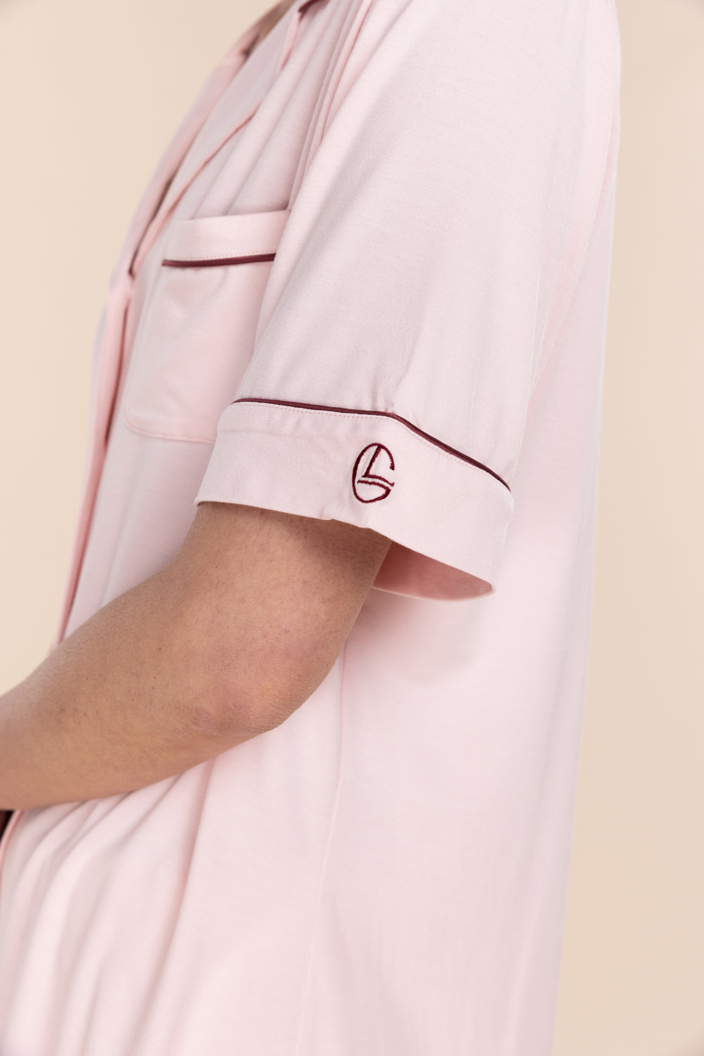 Close-up of a pink shirt with a logo on the sleeve against a beige background