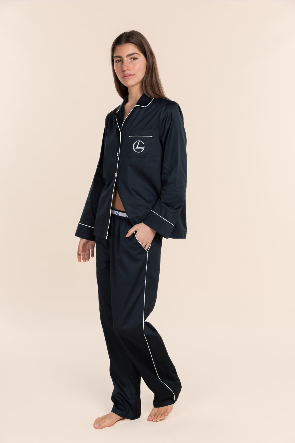 Woman wearing navy blue pajamas with white piping on a beige background