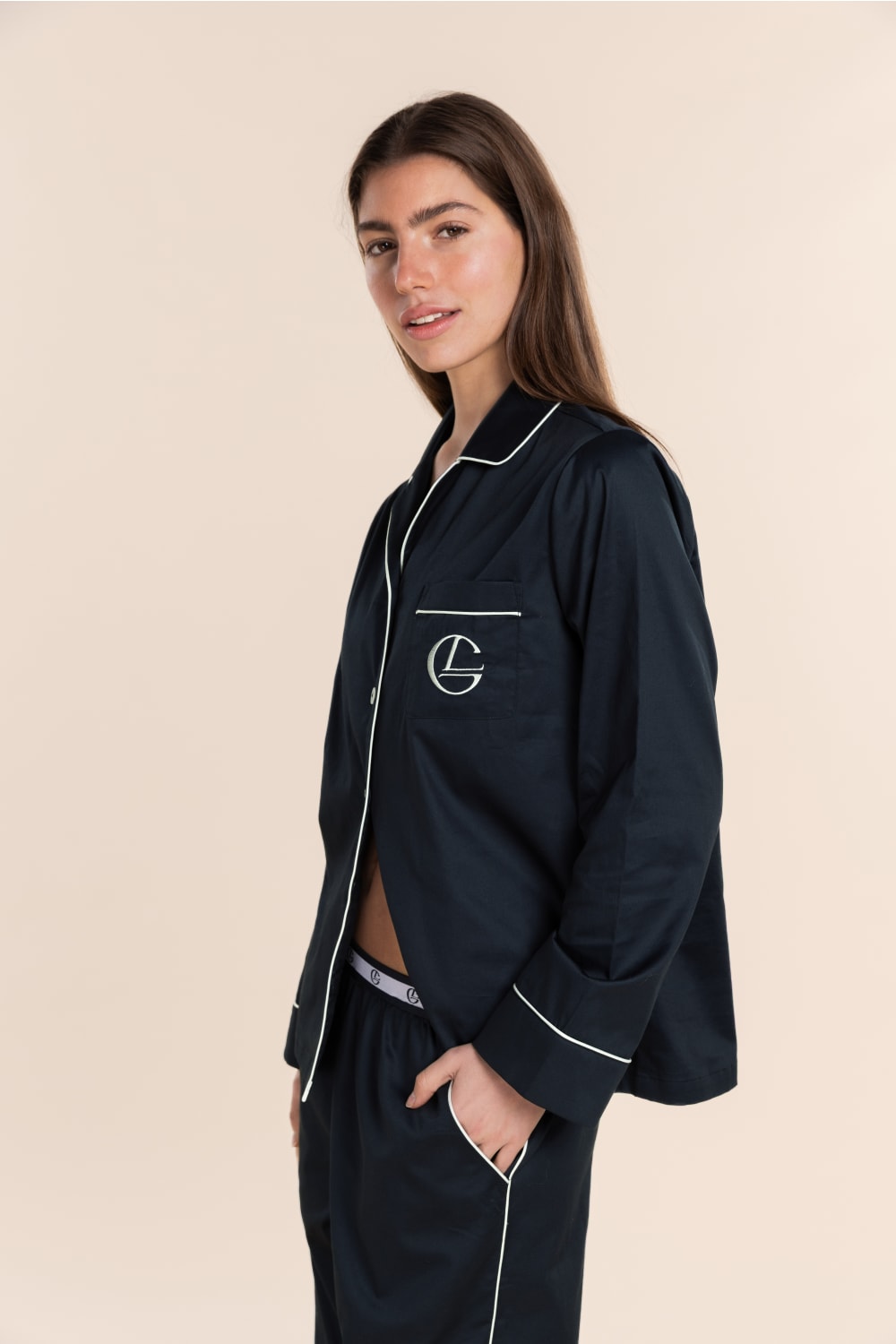 Woman wearing a navy blue pajama set with a logo on a beige background