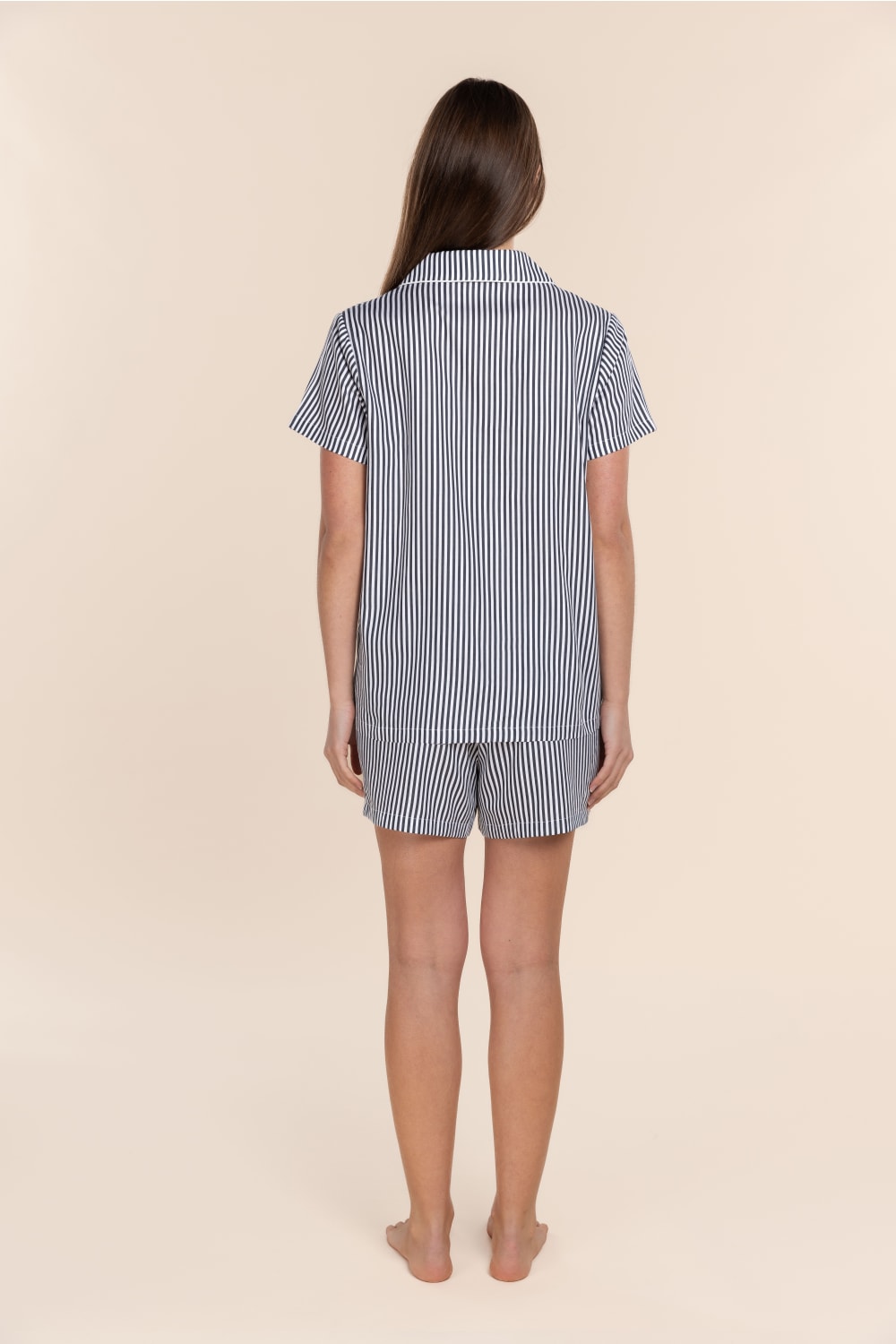 Woman wearing a blue and white striped pyjama set on a beige background