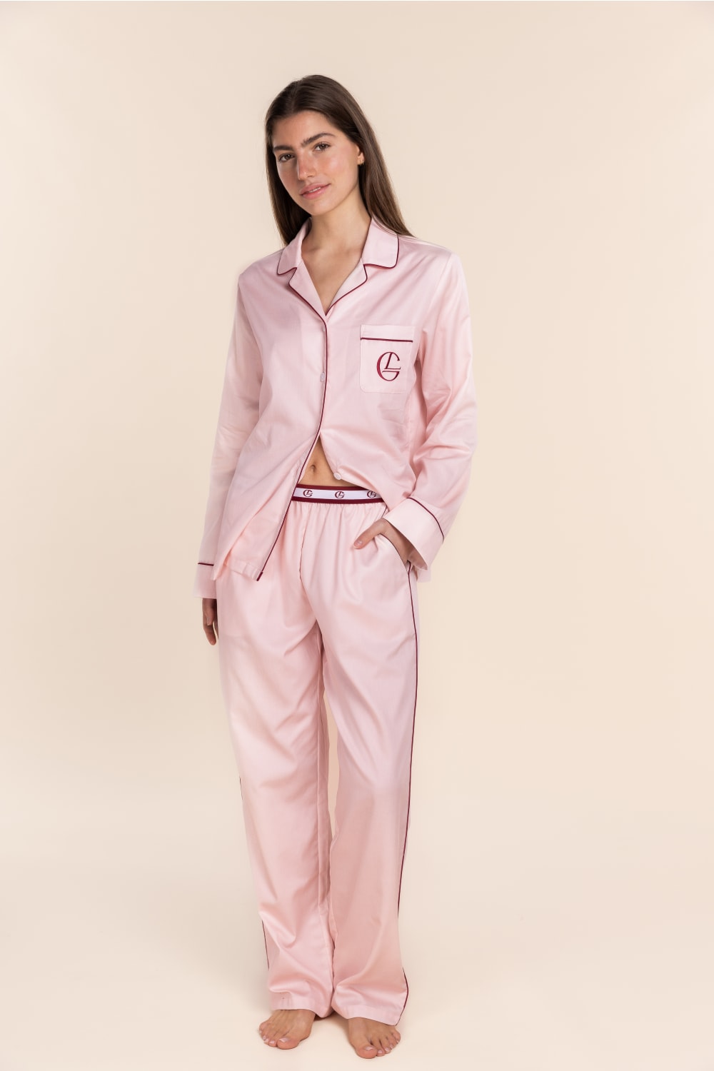 Woman wearing a pink satin pajama set with a monogram on a beige background