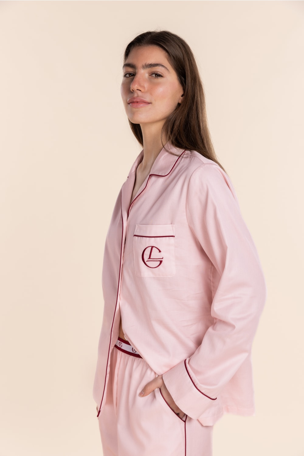 Woman wearing a pink satin pajama set with a logo on a beige background