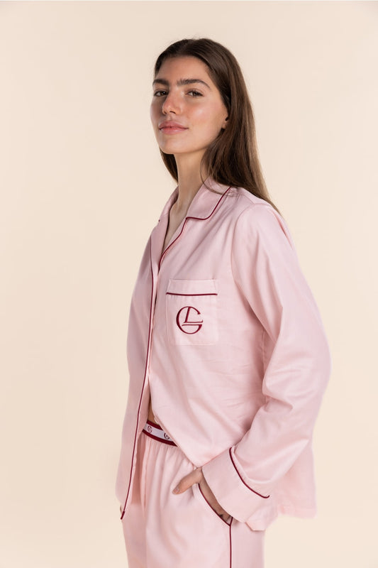 Woman wearing a pink satin pajama set with a logo on a beige background