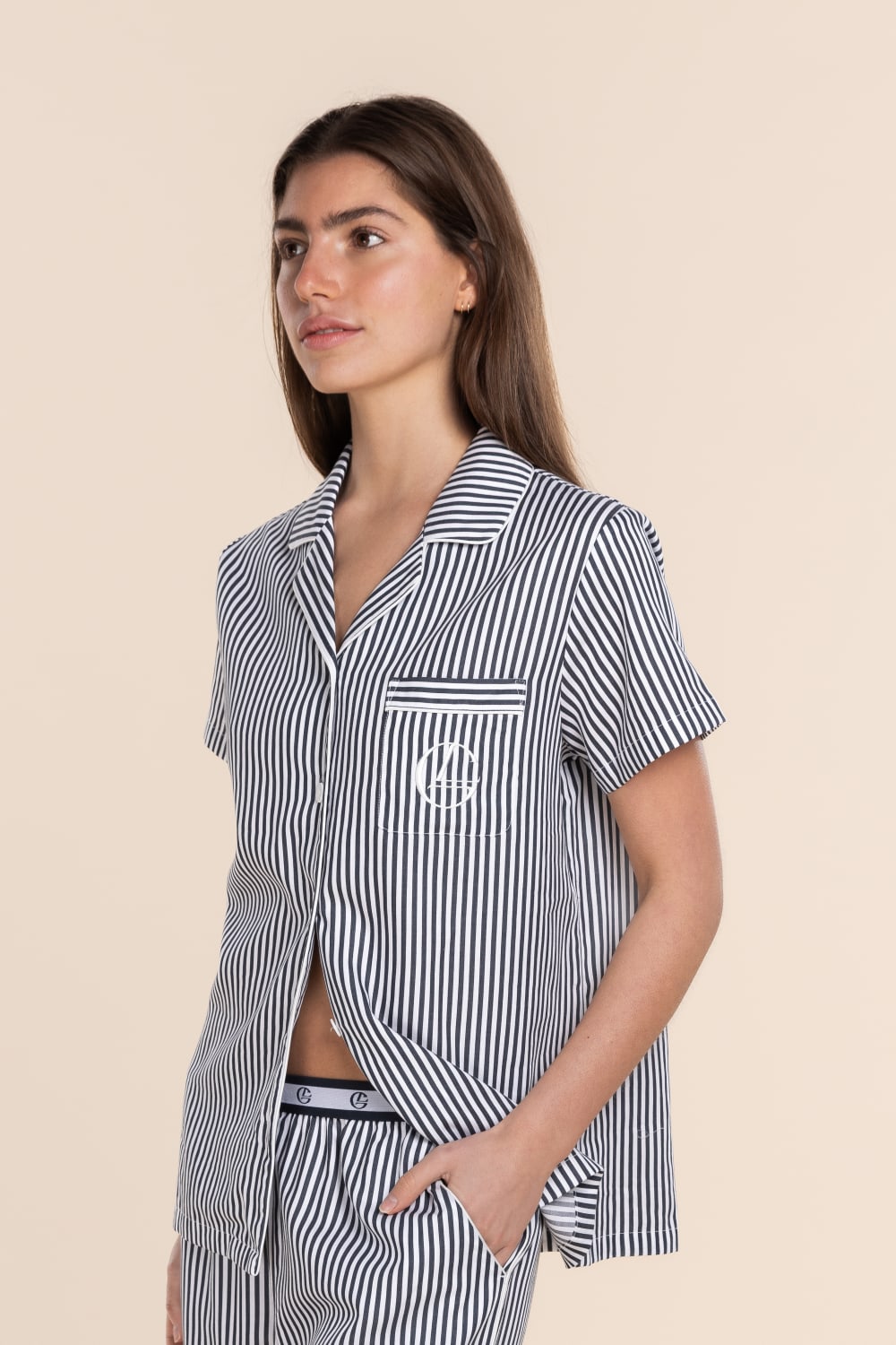 Woman wearing a navy and white striped pajama set with a pocket on a beige background