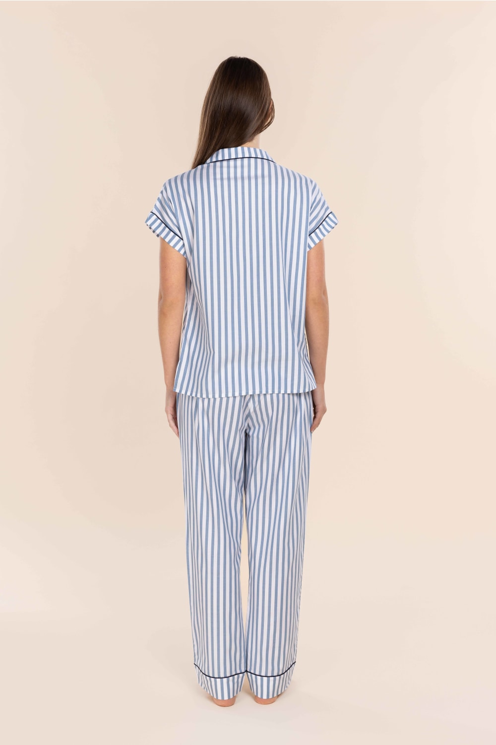 Woman wearing a blue and white striped pajama set on a beige background