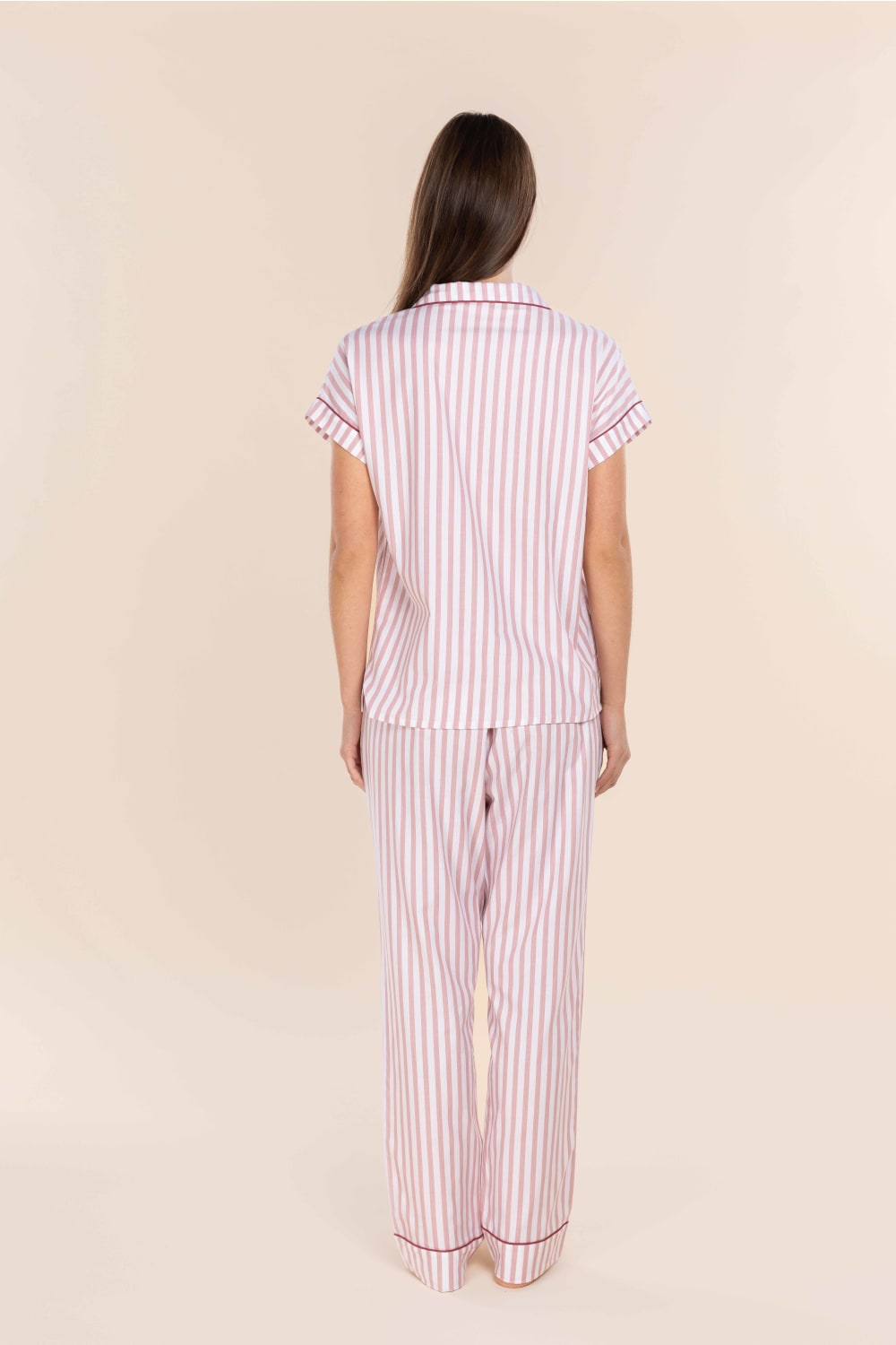 Woman wearing a pink and white striped pajama set on a beige background