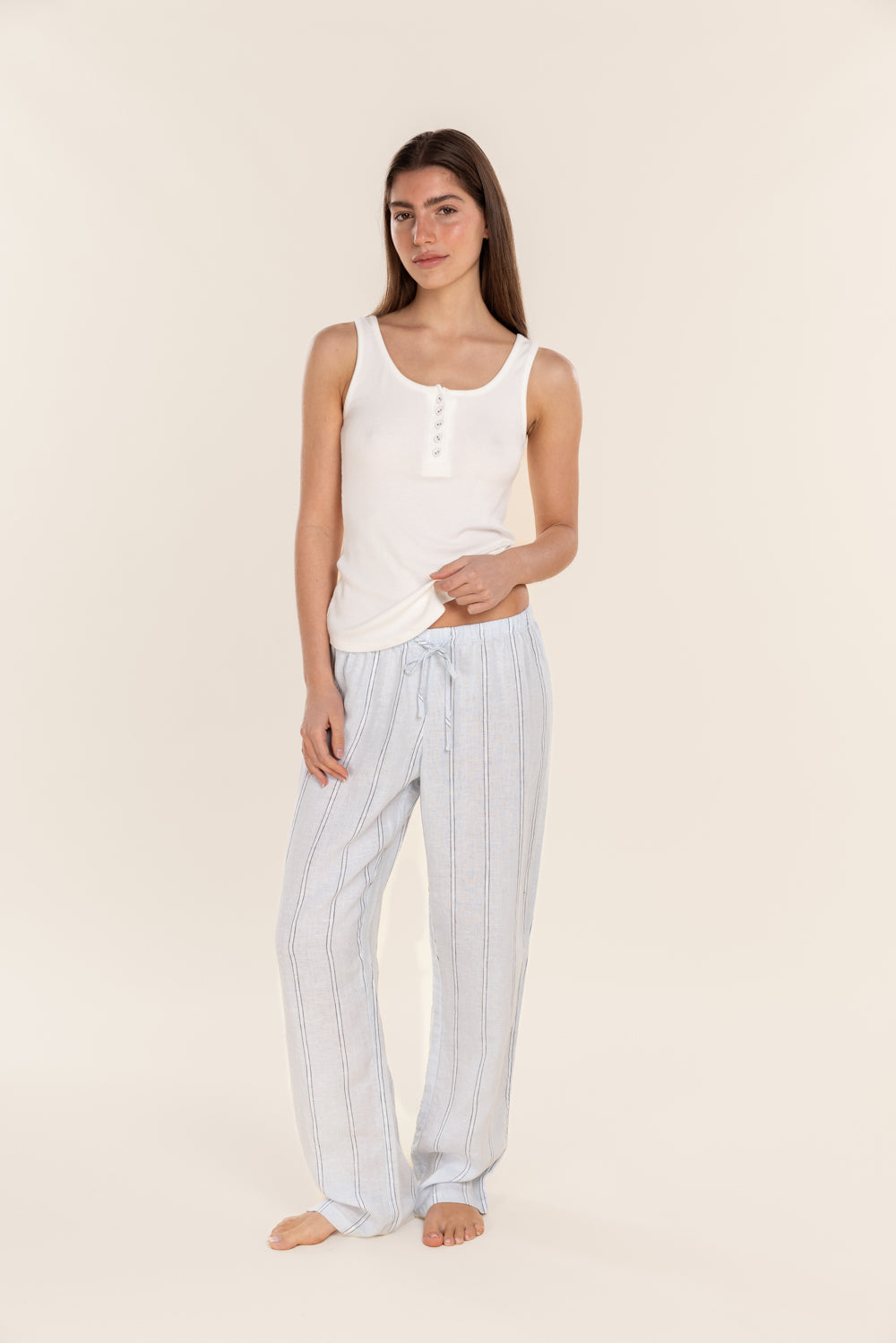 Woman wearing a white tank top and striped pants on a beige background