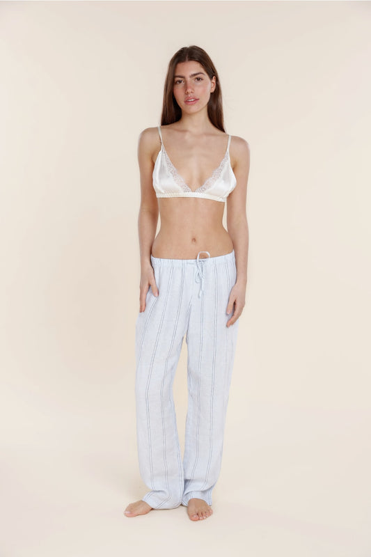 Woman wearing a white bra and light blue striped pants on a beige background