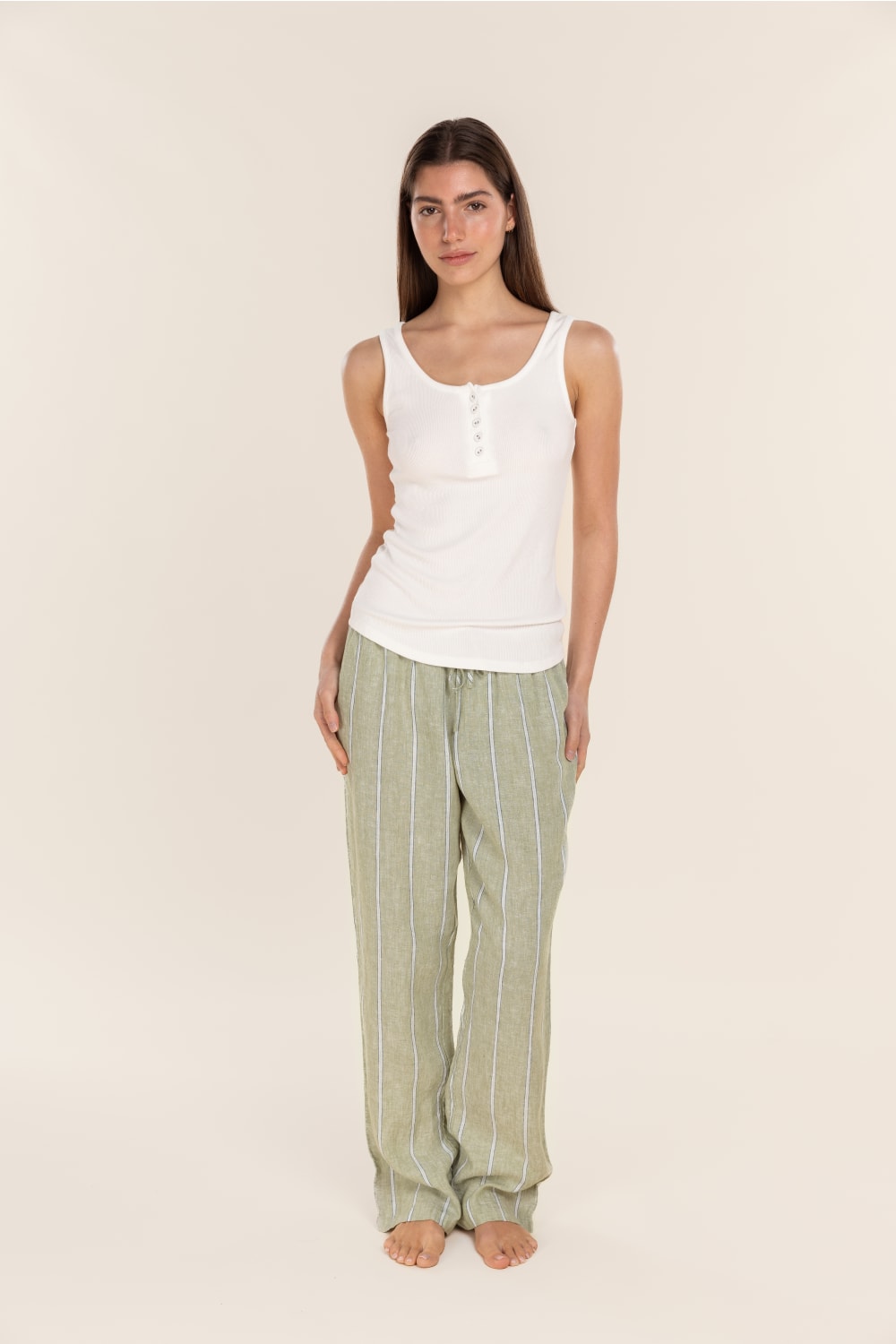 Woman wearing a white tank top and green striped pants on a beige background
